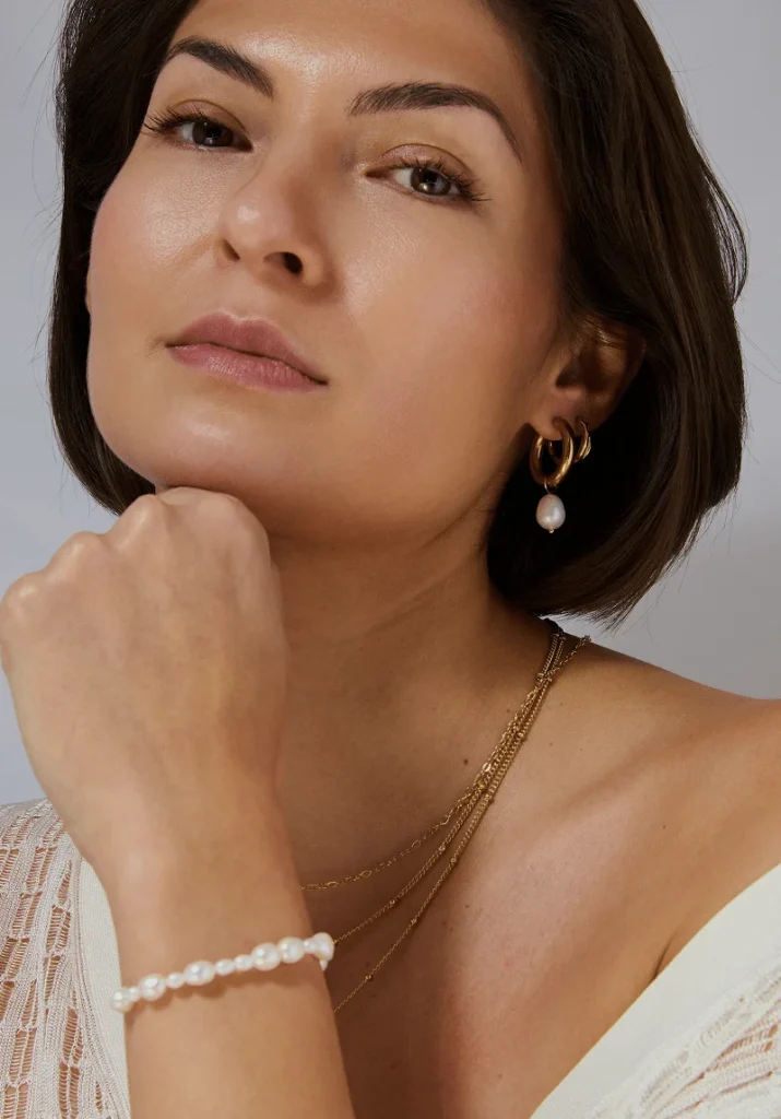 Model wearing Aelva Molten Baroque Pearl Hoops with layered gold chains and a pearl bracelet